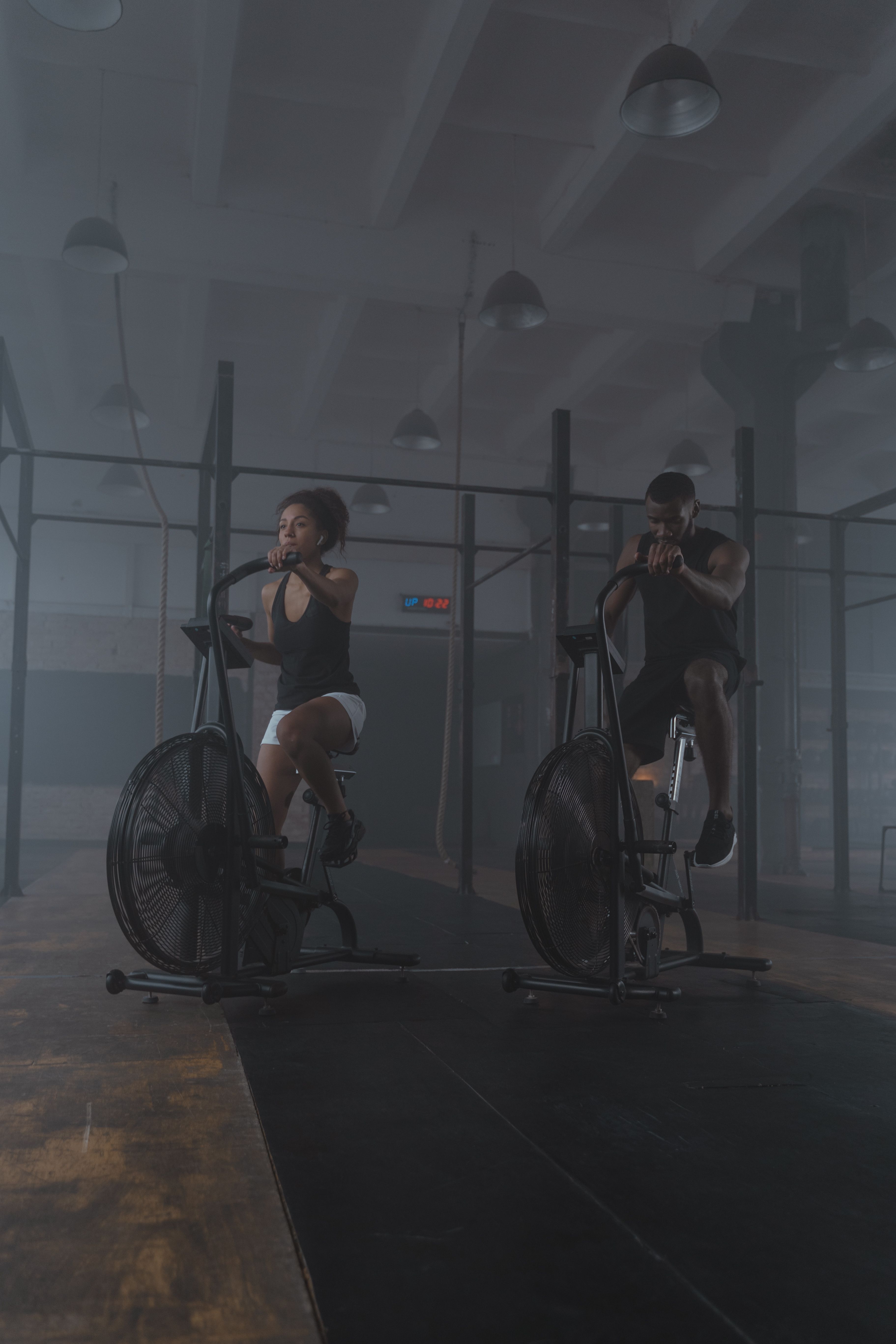 Two clients training side by side on air bikes in a moody, atmospheric gym